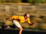 Person rollerblading fast in a yellow shirt and shorts, background is blurred to show motion.