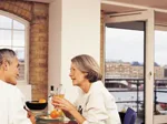 A couple enjoys breakfast together in a cozy dining room with a view through open balcony doors.