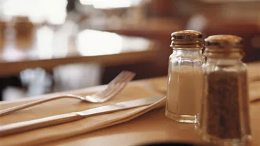 Salt and pepper shakers on a dining table with a fork and knife.