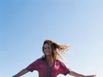 A woman joyfully spreads her arms under a clear blue sky, wearing a floral dress with the wind in her hair.