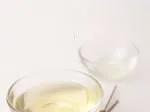 A clear glass bowl of green tea with a smaller empty glass bowl behind, against a plain light background.