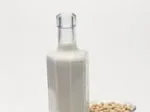 Bottle of soy milk next to a bowl of soybeans on a white background.