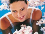 A woman smiles while relaxing in a bath filled with water and floating flowers.