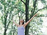 Person in nature with arms raised, surrounded by trees and sunlight filtering through leaves.