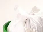 A tied white garbage bag in a green bin against a plain background.
