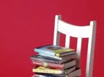 Stack of books on a white chair against a red background.