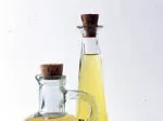 Two glass bottles with cork stoppers filled with light yellow oil against a white background.