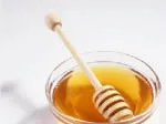 A wooden dipper in a bowl of golden honey on a white background.