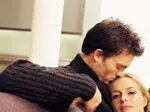 A man kisses a woman's forehead in an intimate, comforting moment, with both seated indoors.