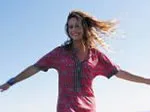 A woman in a red dress joyfully stretches her arms wide under a clear blue sky.
