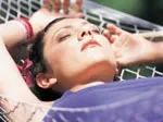 A woman relaxes on a hammock, arms behind her head, eyes closed, enjoying the sunlight.