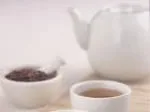 A teapot, cup of herbal tea, and a bowl of loose tea leaves on a table.