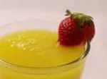 A glass of mango smoothie topped with a fresh strawberry on the rim.