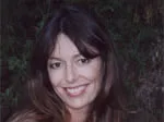Young woman with long brown hair smiling in front of a leafy backdrop.