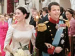 Royal couple in formal attire, bride with bouquet, leaving a ceremony surrounded by guests.