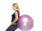 A person leaning against a purple Swiss ball, performing an exercise on a white background.