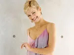 Smiling woman with short blonde hair in a sleeveless pastel dress, standing against a light background.