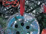 Decorative pie plate ornament on Christmas tree with blue and green colors, red ribbon, and button details.