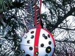 Glittery white Christmas ornament with sequins and red ribbon, hanging on a tree branch.