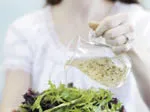 Person pouring dressing over a fresh green salad.