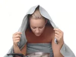 Woman steaming face with towel over head and bowl, illustrating at-home spa trick.