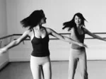 Two women in workout clothes joyfully spinning in a dance studio, expressing freedom and movement.