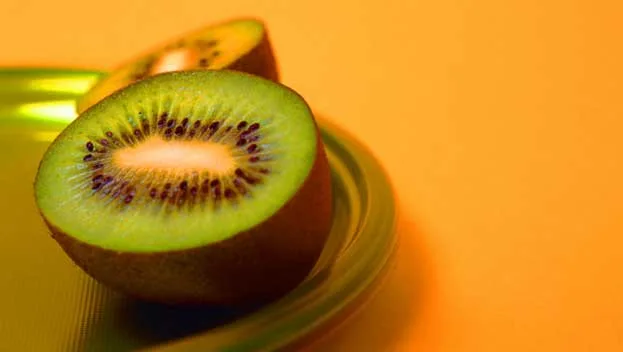 Sliced kiwi fruit on a green plate with an orange background.