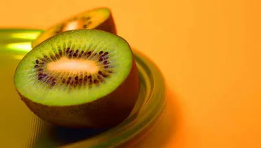 Sliced kiwi fruit on a green plate with an orange background.