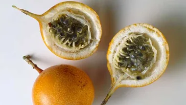 Ripe passion fruits with vibrant orange skin, one whole and one cut open to show seeds, on a plain surface.