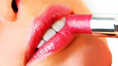 Applying bright pink lipstick to close-up of partially open lips.