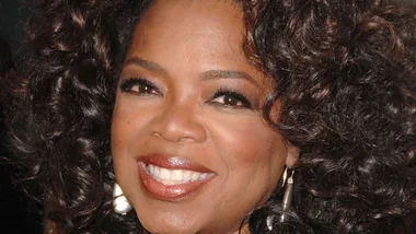 Oprah Winfrey smiling, wearing earrings and curly hair, close-up.