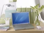 Laptop on a tidy desk with green folders, white flowers, a lamp, and stationery.