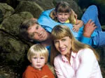 Family portrait of four; parents with young son and daughter, smiling and seated outdoors.