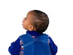 A baby in a blue denim outfit looks upward against a white background.