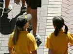 Children in yellow shirts walking on a brick path, part of a walking bus group.