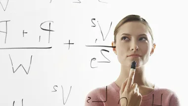 Woman thinking, holding a marker, in front of a whiteboard filled with mathematical equations.
