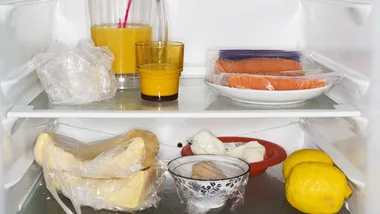 Fridge interior with drinks, packaged salmon, plastic-wrapped cheese, lemons, and various food items on two shelves.