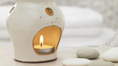 Ceramic aroma diffuser with a lit tealight candle, surrounded by smooth stones, creating a calming ambiance.