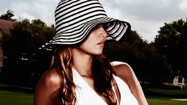 Woman in a striped sun hat and white top, outdoors with trees in the background.
