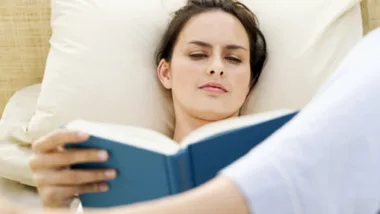 Woman relaxing on a bed while reading a book.