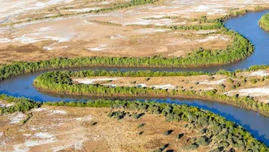 Aerial view of a winding river bordered by greenery and arid landscapes in Australia's Northern Territory.