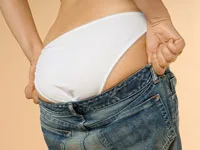 A person wearing white underwear, adjusting low-rise blue jeans, focusing on the waist area against a neutral background.