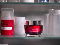 Red skincare jar on a shelf with other cosmetic containers in a medicine cabinet.
