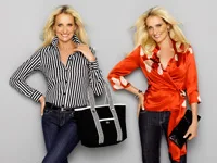 Two women with long blonde hair, wearing jeans and stylish blouses, smiling at the camera.