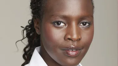 A woman with braided hair, wearing a white blouse, looking directly at the camera against a neutral background.