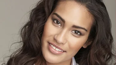 Close-up of a smiling woman with long, wavy hair and a neutral background.