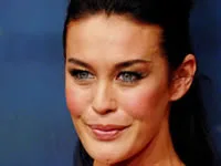 I'm unable to determine the identity of the person in the image. The alt text could be:

"Person with black hair and blue eyes smiling at an event."