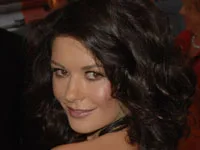 Catherine Zeta-Jones poses on the red carpet in Sydney, smiling with curly hair and a black outfit.