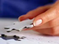 Hand holding a silver puzzle piece above a table, symbolizing problem-solving.