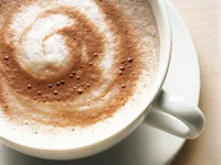 A creamy cappuccino with a swirl of frothy milk and cocoa powder in a white cup, placed on a saucer.